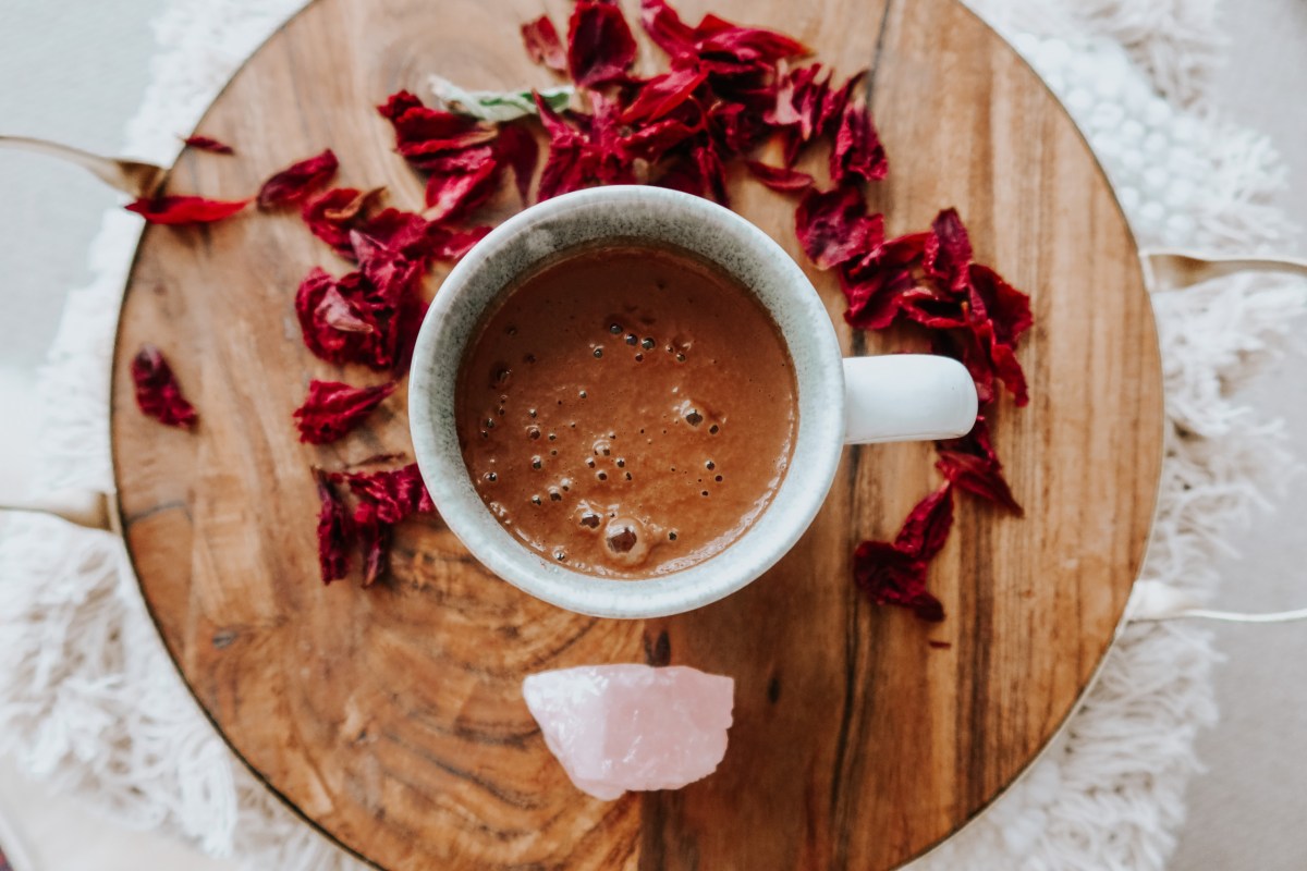 Cacao in a cup on a wooden plate, with roses around it and a rose quartz in front of it